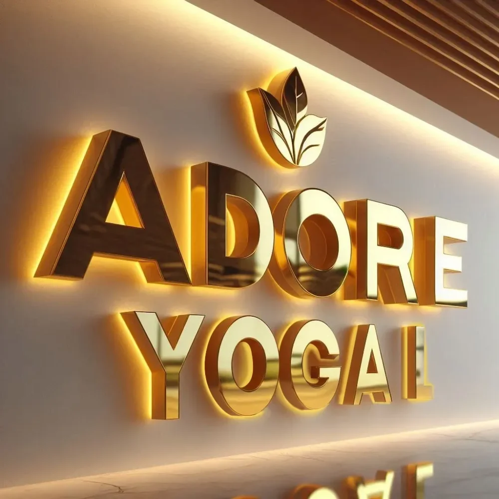 A picture of a Custom Backlit Sign mounted on a wall. The product says ADORE YOGA. The product is gold and illuminated.