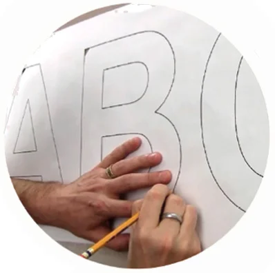 A photo from the blog post How to install dimensional signs showing how to align the template on the wall. There is a man marking with a pen where the letters will be pasted.