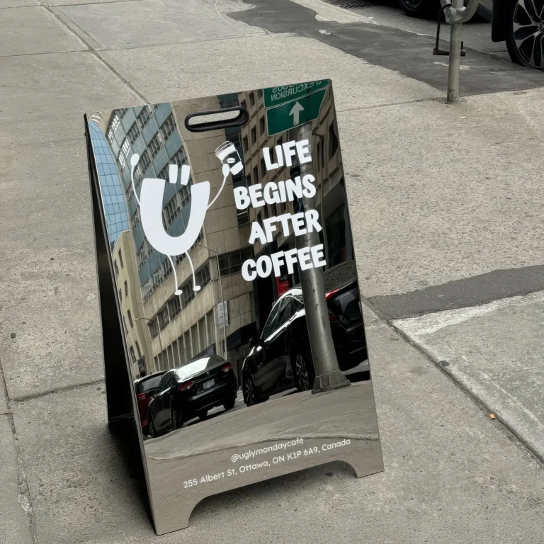 Mirrored chrome A-frame sidewalk sign for a coffee shop, featuring a playful logo and white text reading 'LIFE BEGINS AFTER COFFEE'.